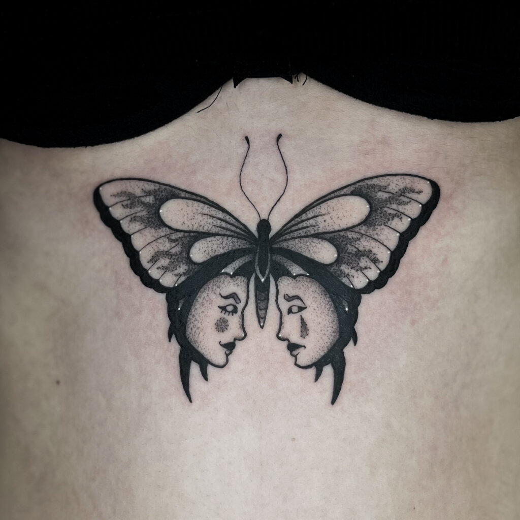 This stunning butterfly tattoo features two human faces integrated into the wings, creating a mesmerizing illusion. The fine line shading and bold black ink details enhance the depth and elegance of the desgin. Placed on the upper back, this tattoosymbolizes transformation, duality and self-reflection. A perfect choice for those seeking a unique and artistic tatoo with deep meaning.